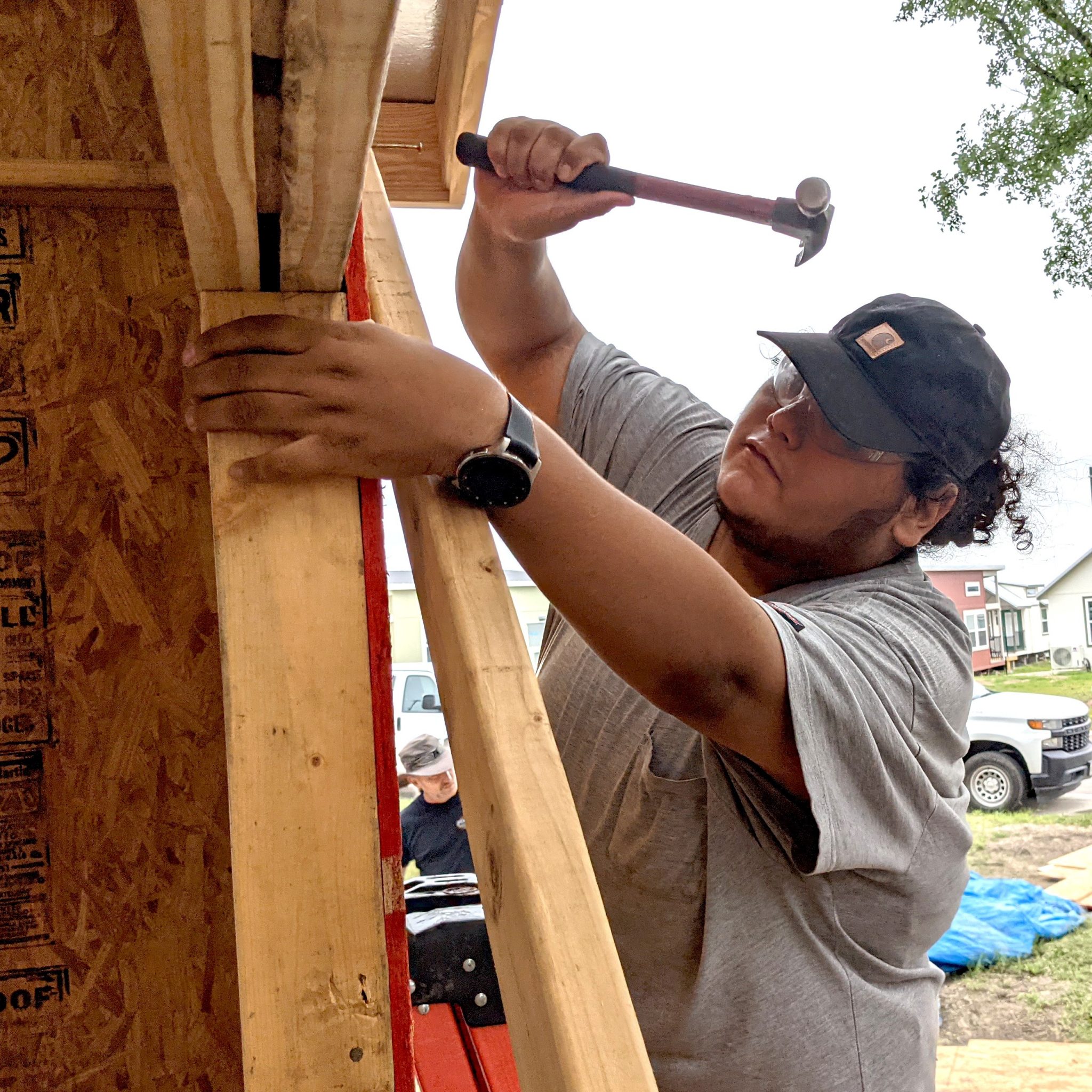Close up of a YouthBuild Austin participant using a hammer and nail to build a house.
