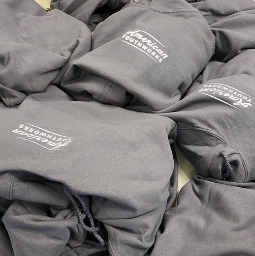 Folded hoodies with the American YouthWorks logo screenprinted on them.